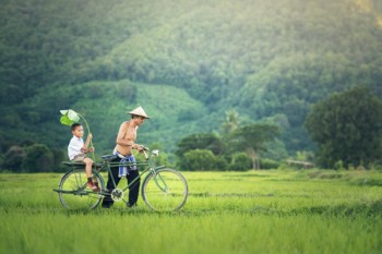 Padre lleva a su hijo montado en bicicleta por el verde campo de Camboya