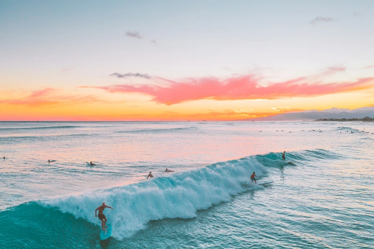 Atardecer en el mar de Hawai con gente surfeando.