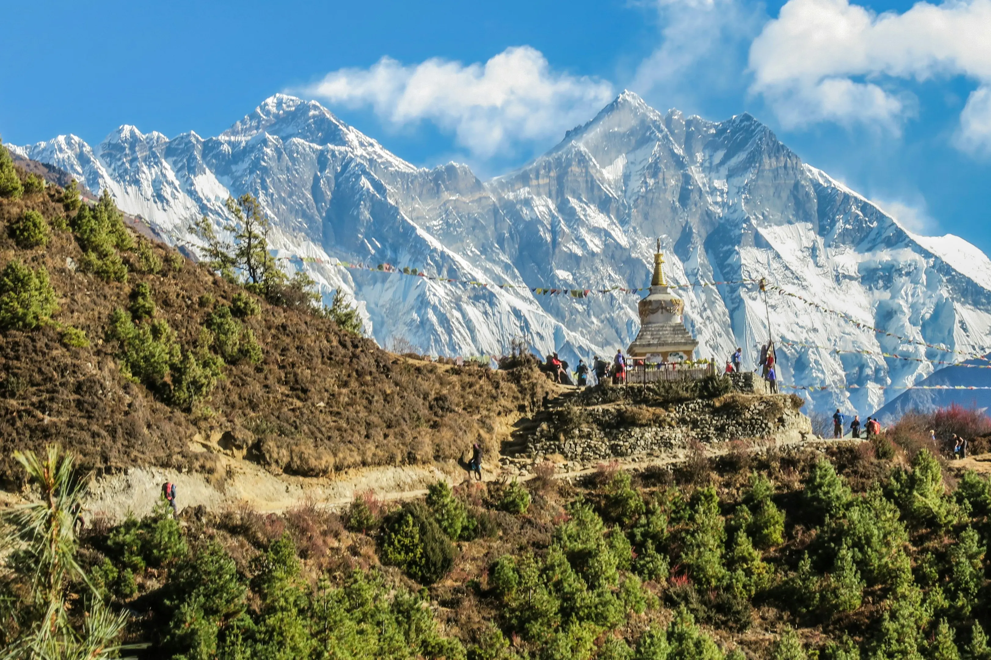 Buddhistische Stupa mit Gebetsfahnen und Trekkern auf dem Weg zum Everest, Nepal, mit dem Himalaya im Hintergrund